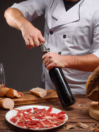 Pig leg on wooden table. Jamon. Spain jamon serrano. Traditional Spanish ham in restaurant interior. Whole jamon on wooden stand. Gourmet ham. Chief open wine bottle. Vertical imageの写真素材