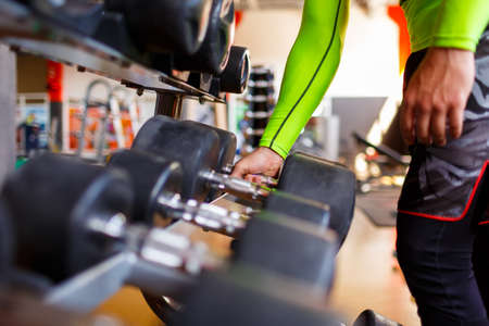 The hand of a strong man takes a heavy dumbbell in the gymの写真素材