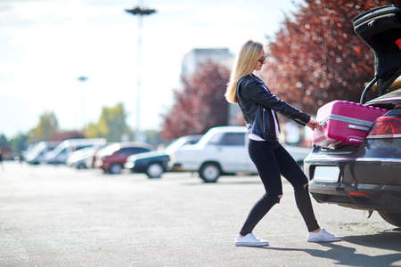 The girl takes out her pink suitcase from the trunkの写真素材