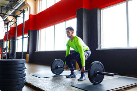 A young bearded man is training with a barbell in the gym.の写真素材