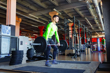 A young bearded man is training with a barbell in the gym.の写真素材