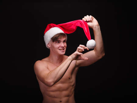 Attractive, funny young man pulling off Santa cap on a black background. Christmas concept.の写真素材
