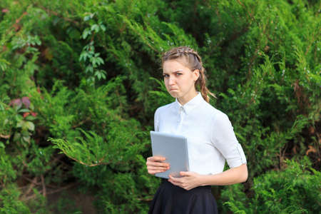 A young brunette girl sits in a park with a tablet.