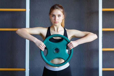 Beautiful young girl is engaged in a gym with a pancake from the bar.の写真素材