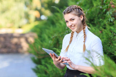 A young brunette girl sits in a park with a tablet.の写真素材