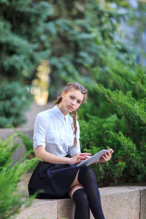 A young brunette girl sits in a park with a tablet.の写真素材