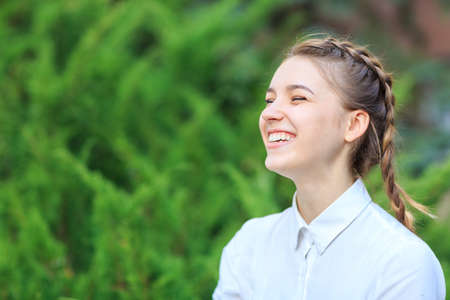 Beautiful young girl in a park on a background of fir branches.