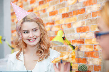Smiling office lady, at lunchtime and eating pizza. Festive atmosphere.