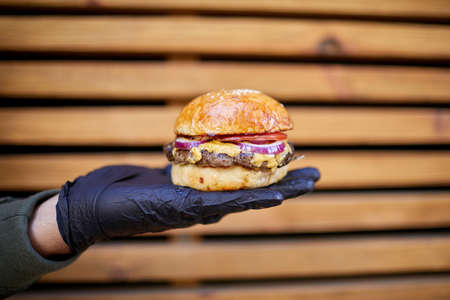 Juisy burger with beef in male hand on the wooden background. Food concept.
