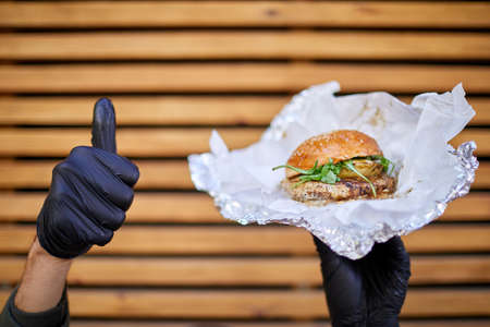 Juisy burger with beef in male hand on the wooden background. Food concept.の写真素材