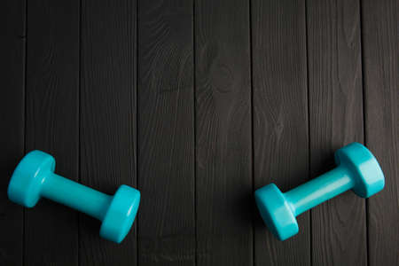A big blue dumbbells for sports exercises. Sports equipment on a dark gray wooden parquet. Close-up...
