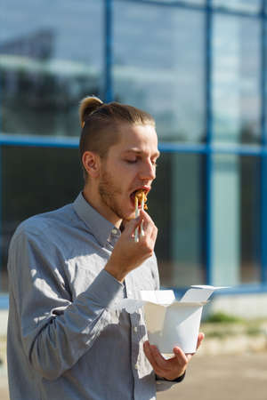 Handsome man with chinese noodles in box with shrimp, vegetables and sesame with soy sauce. Food concept.の写真素材