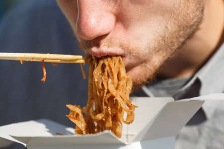 Handsome man with chinese noodles in box with shrimp, vegetables and sesame with soy sauce. Food...