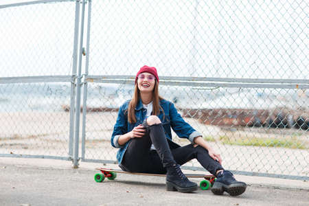 Pretty girl sitting on a skateboard outdoors on the nature background.