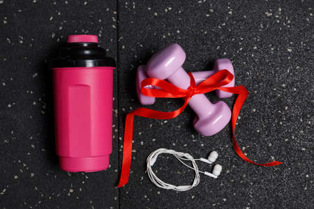 Small red dumbbells for fitness on a black background with a floor with a water bottle and headphonesの写真素材