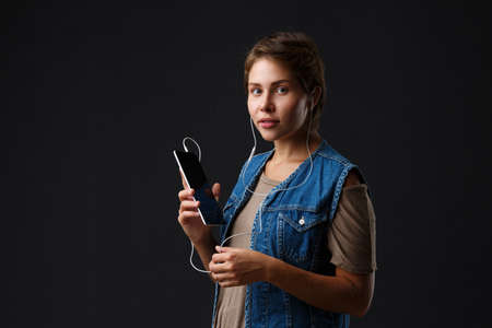 Beautiful girl listens to music with her phone on a black background.