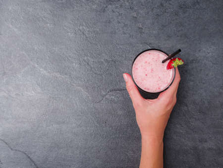 Tasty sweet strawberries and fruits yogurt in a glass on females hand on a gray marble background....