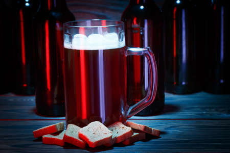 A large glass of dark beer with a bottle on a brown background with bottles and a snackの写真素材