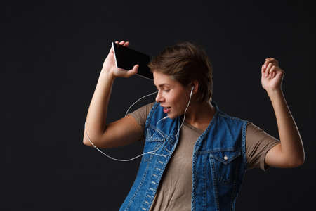 Beautiful girl listens to music with her phone on a black background.の写真素材