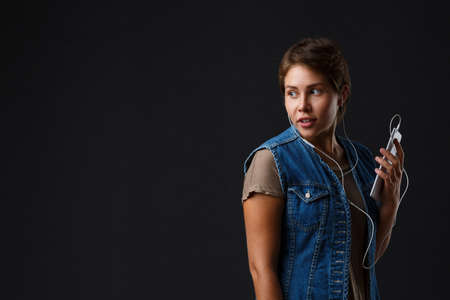 Beautiful girl listens to music with her phone on a black background.の写真素材