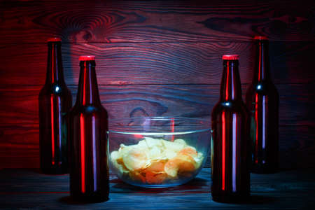 A bowl of a snacks in the middle of the four bottles on the wooden backgroundの写真素材