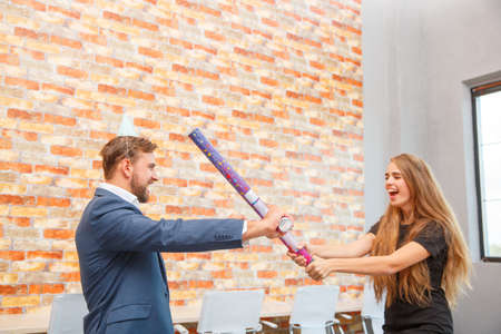 In the office at a corporate party, a man and a girl are fooled by sticks from under confetti.