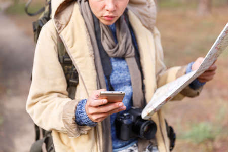 A young girl in the woods is looking for a road map and using a phone.