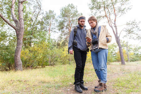 Young couple of tourists in the forest looking at the phone.の写真素材