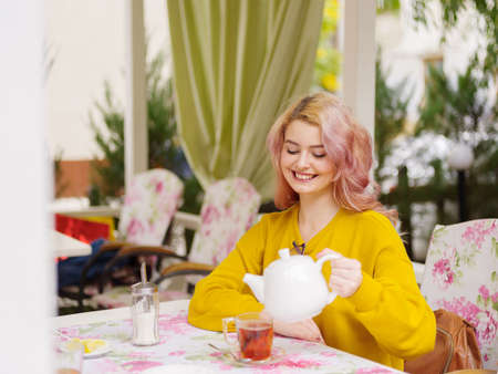 Beautiful young blonde in a yellow sweater at a table in a cafe.の写真素材