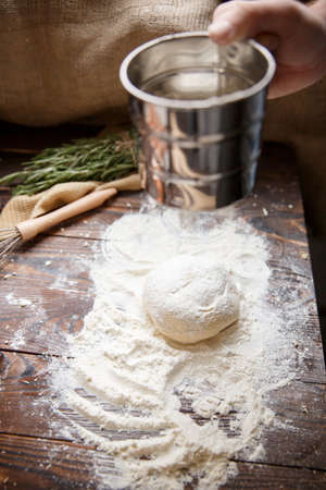 A piece of dough with flour on the table and above it someone holding a mug of water.