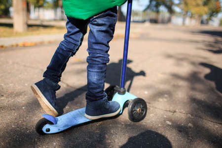 Boy in autumn playing in the street smiling playing with a scooterの写真素材