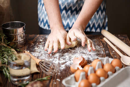 A white man in a blue sweater makes a dough on the kitchen table near the products.