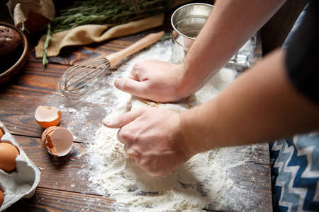 Two hands of a white man press a piece of unleavened dough to the kitchen table. View from above.