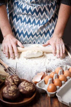 A white man in a striped apron rolls out the dough on the kitchen table.の写真素材