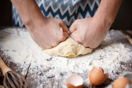 The European chef presses his fists on the dough that lies on the table with flour.