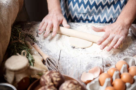 A white man with a wooden rolling pin rolls out a small flat cake made of unleavened dough.