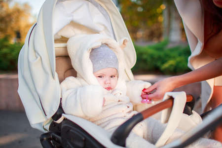A small child is sitting in a stroller and his mother is standing next to him. Outside.の写真素材