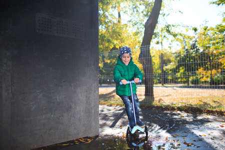 The boy skates on a scooter near a puddle. Outside.の写真素材