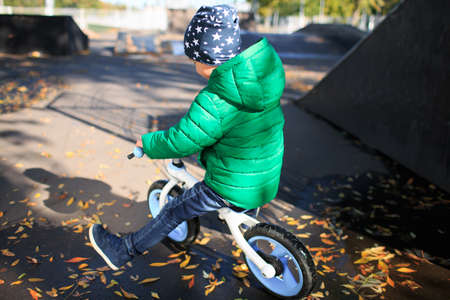 A boy in a green jacket rides a bicycle near a puddle in warm autumn weather.の写真素材