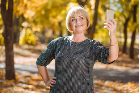 An attractive middle-aged woman walking in an autumn park with gadgets on a blurred background.の写真素材