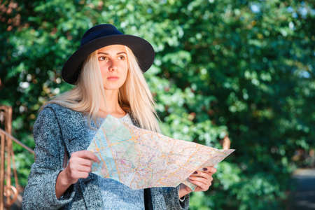 A young girl holds a map in her hand and looks thoughtfully to something. Outside.の写真素材