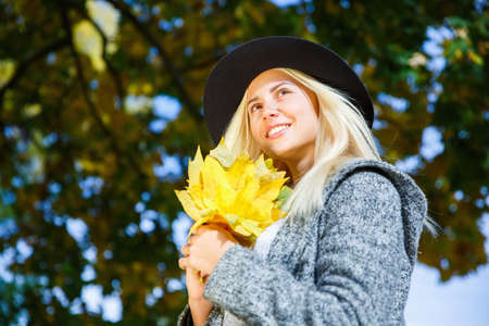 The lovely blonde is holding yellow foliage in her hands.