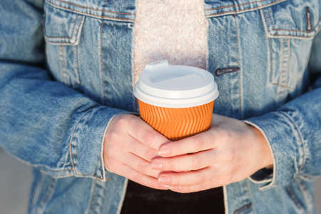 A serving of fragrant coffee in an orange plastic cup in the girl's hands.
