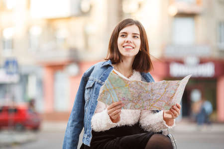 A girl with a card sits on a bench, looks away and smiles.