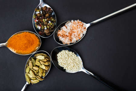 View from above. Spoons are spread out in a circle with spices from a mixture of pepper, salt, paprika, sesame and sunflower seeds.の写真素材