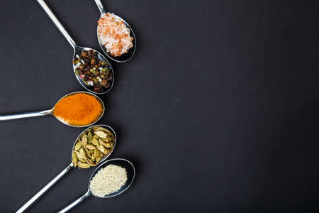 Metal spoons with different spices are arranged in an arc on a black background. View from above. Inside. Close-up.の写真素材