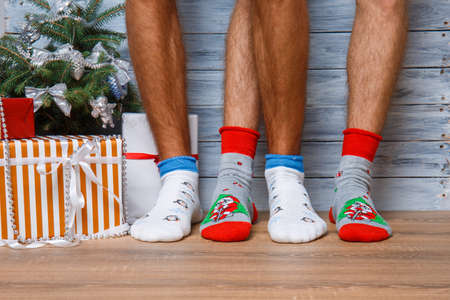 Closeup image of male feet in woolen socks on a wooden background. Standing next to the gifts and the Christmas tree. Hairy men's legs in New Year's socks.の写真素材