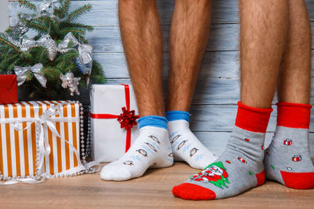 Closeup image of male feet in woolen socks on a wooden background. Standing next to the gifts and the Christmas tree. Hairy men's legs in New Year's socks.の写真素材