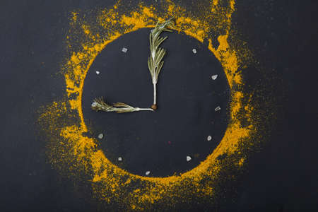 Composition of a clock from spices and green grass on a black background.