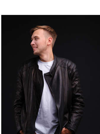 The guy in the black jacket looks away and smiles. On a black background.